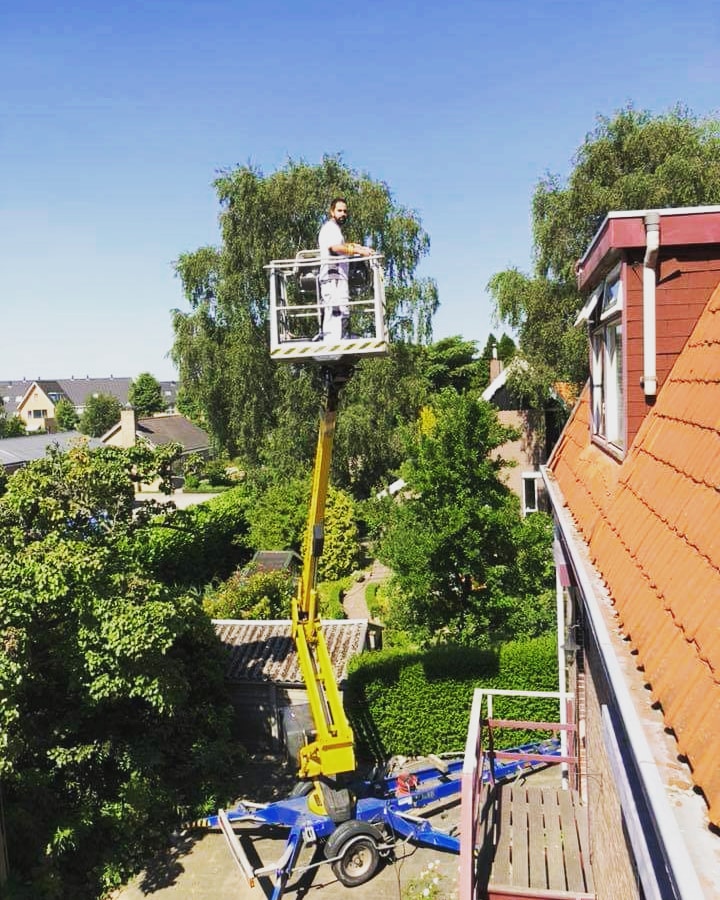 Schilder in een hoogwerker bij een dakkapel met oranje dakpannen