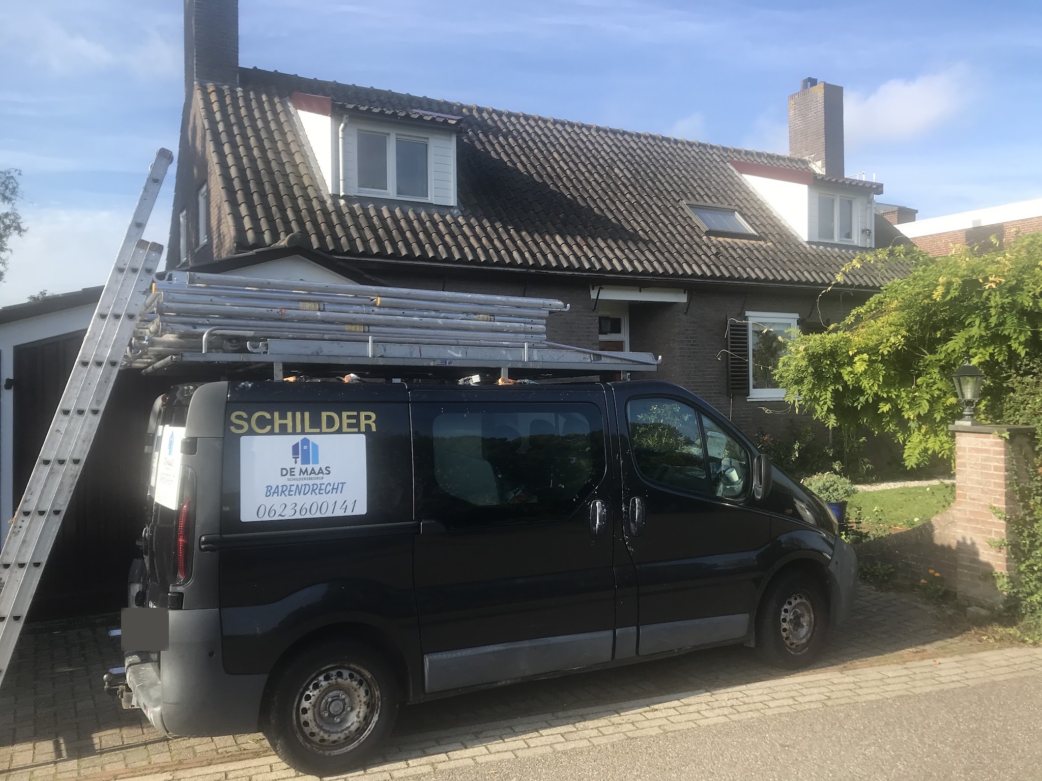 Werkbus met ladders en steigerdelen op het dak voor een woning