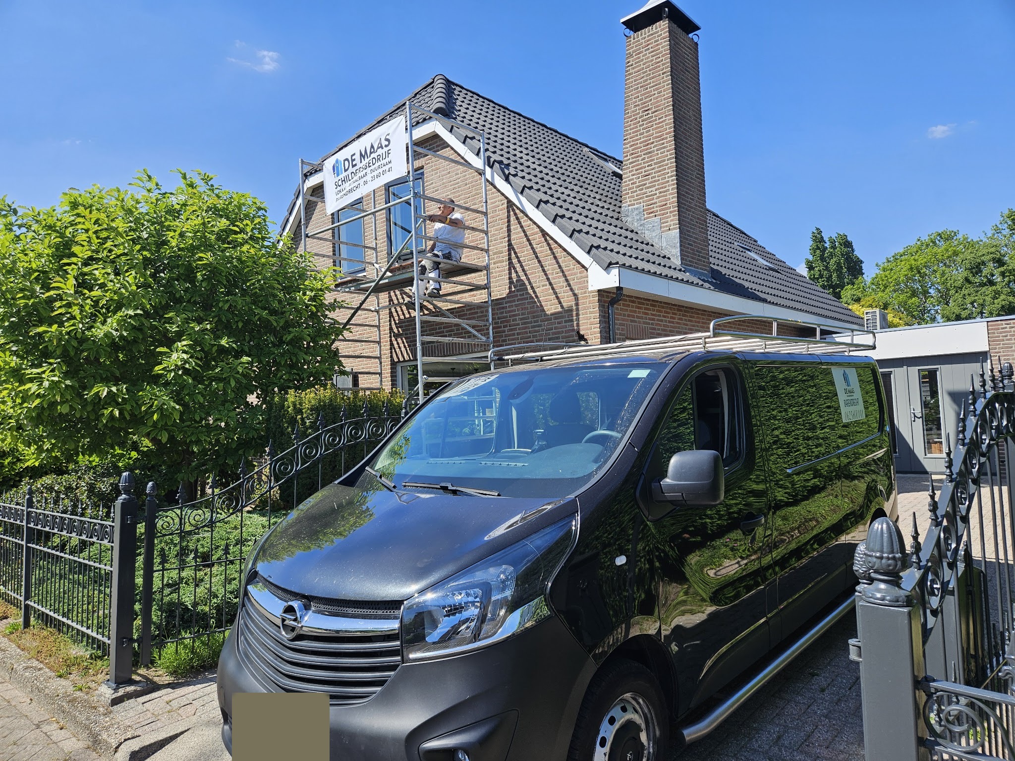 Werkbus voor een woning met banner op de steiger en een schilder aan het werk onder de dakrand