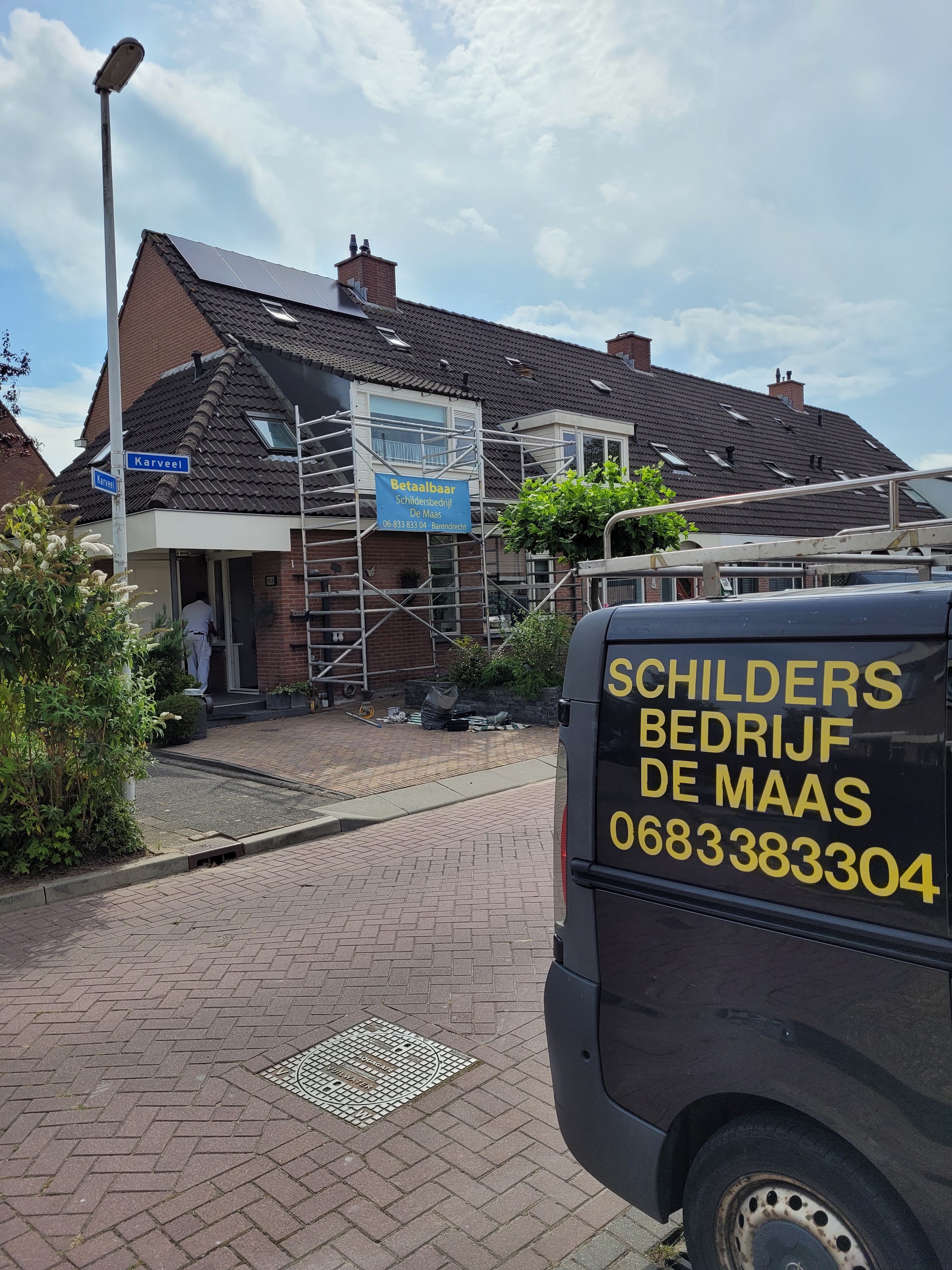 Steiger met het blauwe banner van Schildersbedrijf De Maas aan een rijtjeshuis, de zwarte bus met belettering op de voorgrond