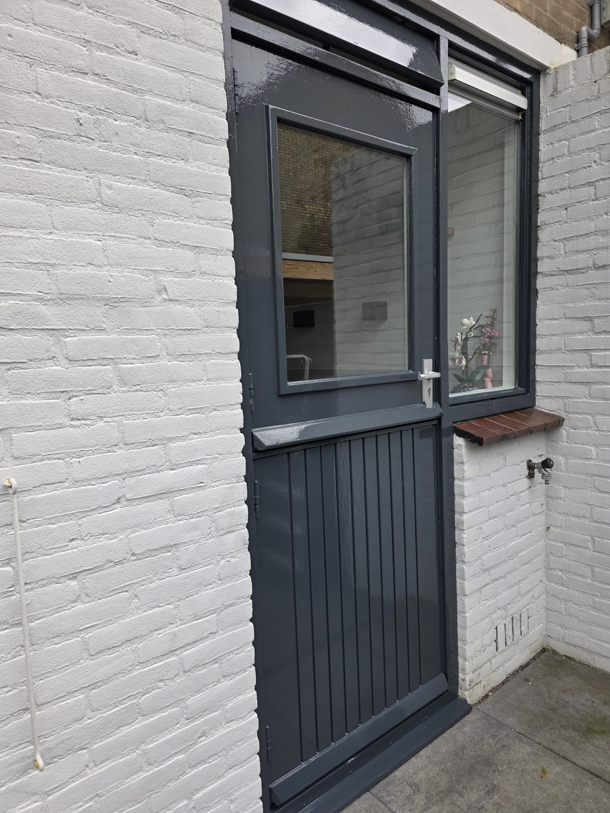 Pas geschilderde donkergrijze achterdeur met kozijn in een witte bakstenen muur