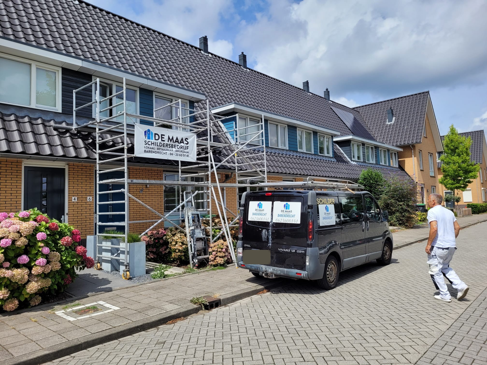 Straat met steiger en banner van De Maas, de bus en een schilder in het wit