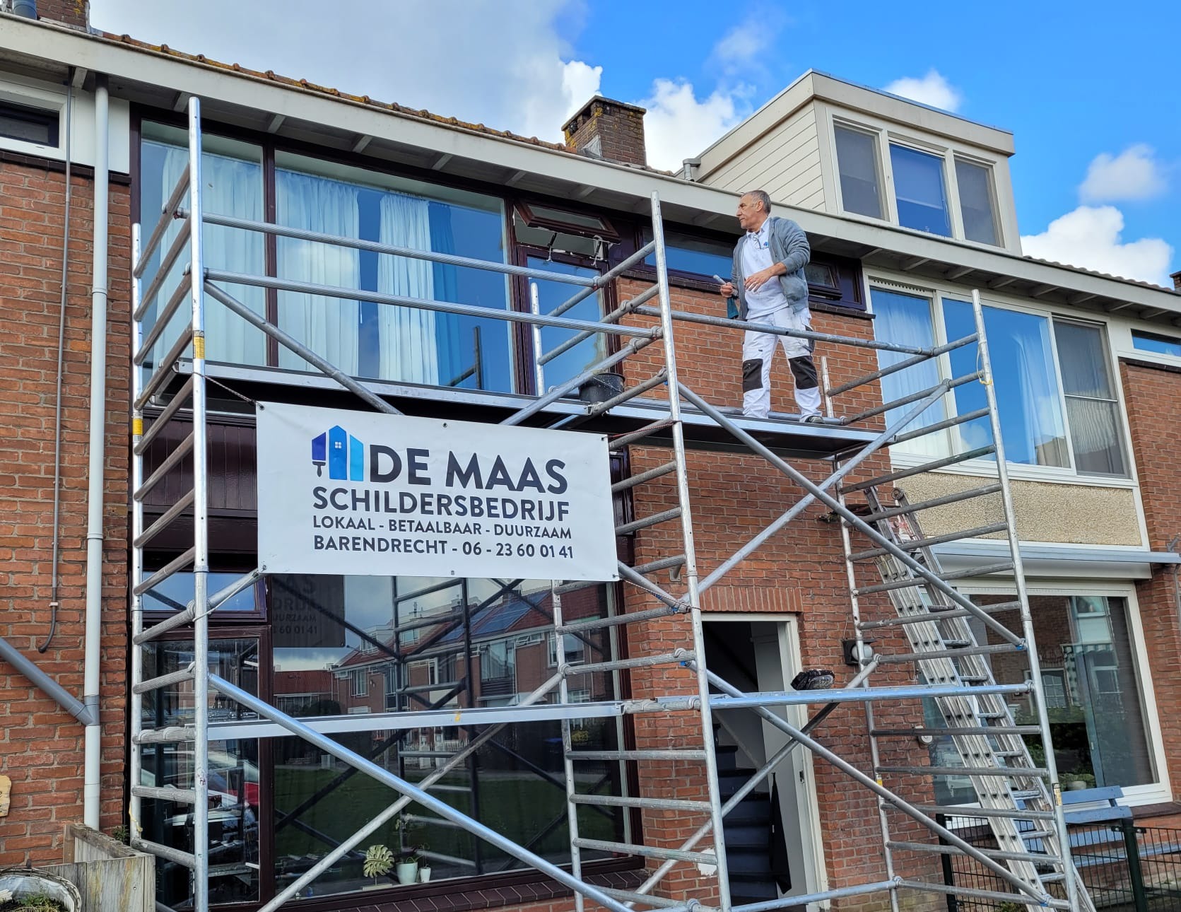 Hashem op de steiger, met het grote banner De Maas Schildersbedrijf, lokaal, betaalbaar, duurzaam, Barendrecht