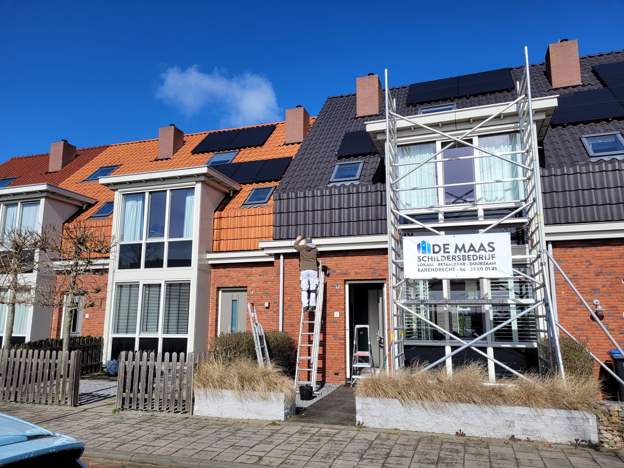 Rijtjeshuizen onder een blauwe lucht met de steiger en het banner van De Maas aan de gevel