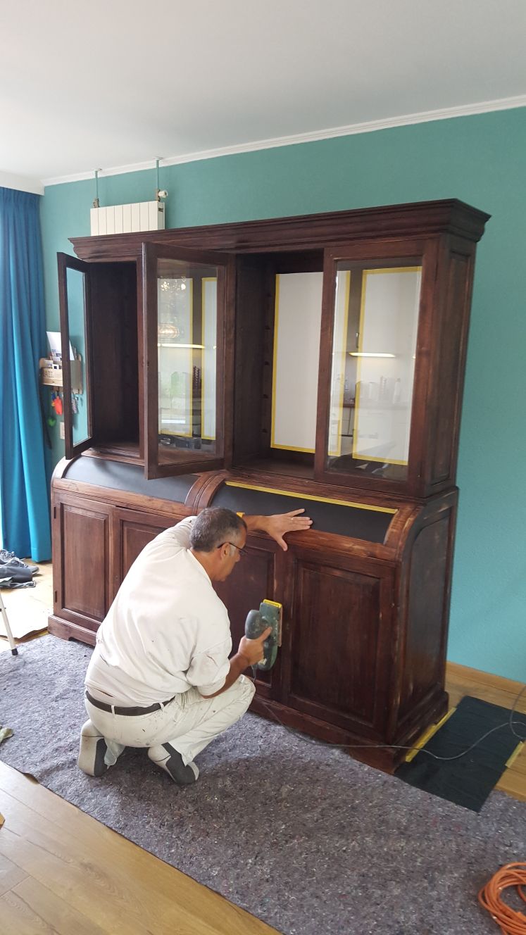 Schilder schuurt een donkere houten kast, de glasdelen afgeplakt